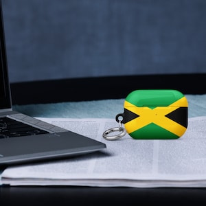 May include: A black and silver laptop computer is open on a white page with black text. A black and silver keychain with a silver ring is attached to a black and green case with the Jamaican flag printed on it.