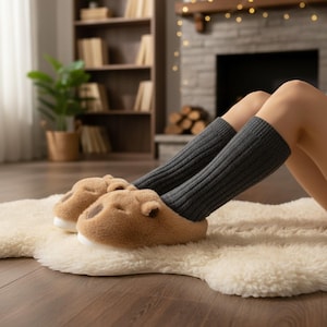 May include: A cozy scene featuring brown bear-shaped slippers with white soles and gray leg warmers. The slippers rest on a cream-colored, fluffy rug, suggesting comfort and relaxation. The background includes a fireplace and a bookshelf.