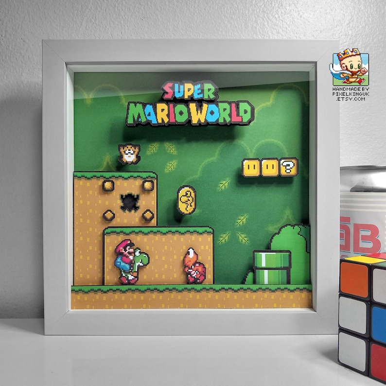 Front view of the Super Mario World Yoshi’s Island shadow box in a white frame, showing Yoshi, a red enemy, blocks and a green pipe.