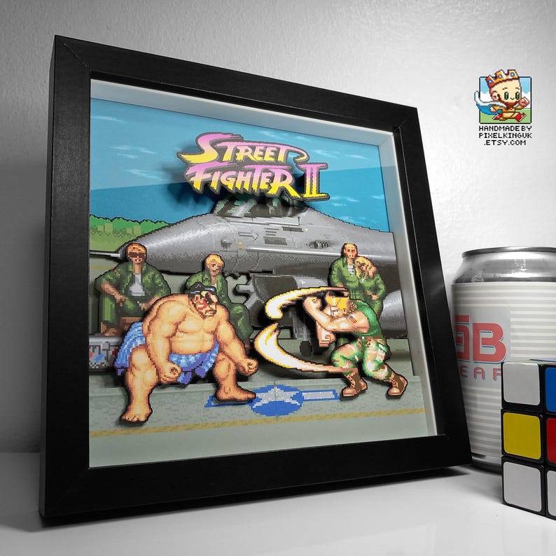 Angled view of a framed Street Fighter II pixel art shadow box showing E. Honda facing Guile on the airbase stage.