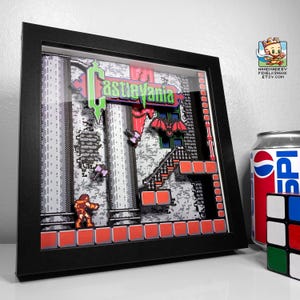 Può includere: Un'opera d'arte 3D incorniciata con una scena pixelata del videogioco Castlevania. L'opera include il logo del gioco, un personaggio, pipistrelli e una scala. La cornice è nera e l'opera è ambientata su uno sfondo grigio e rosso.