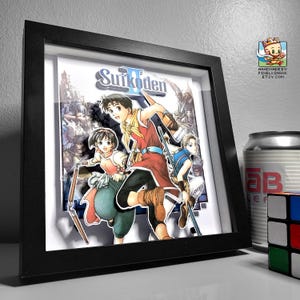 Puede incluir: Una obra de arte 3D enmarcada con personajes del videojuego Suikoden II. La obra, en un marco negro, presenta personajes de estilo anime en colores vibrantes. Una lata y un cubo de Rubik son visibles en el fondo.