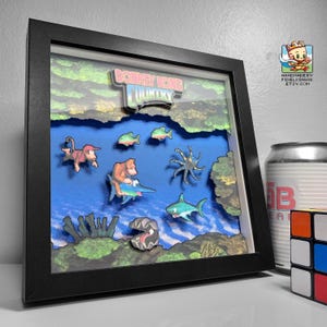 May include: A black framed 3D diorama of the Donkey Kong Country video game. The diorama features a blue background with a variety of characters and objects from the game, including Donkey Kong, Diddy Kong, and a shark. The diorama is handmade and is a great way to show your love for the classic video game.