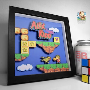May include: A framed pixel art piece featuring the video game character Alex Kidd in Miracle World. The art is in a black frame and includes a 3D effect. The title "Alex Kidd in Miracle World" is featured in the art.