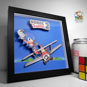 Pode incluir: Uma imagem em pixel art 3D emoldurada em preto de Sonic the Hedgehog voando em um avião vermelho. O título "Sonic the Hedgehog 2" está no canto superior direito da imagem.