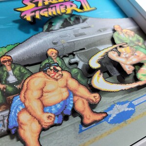 Close-up of the layered artwork showing E. Honda and Guile in front of a military jet.