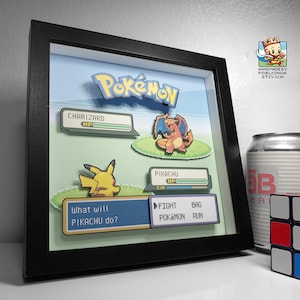 以下が含まれることがあります： ポケモンバトルのシーンを描いた、額装された3Dアートワーク。アートワークには、ポケモンのロゴ、リザードンとピカチュウ、バトルインターフェース要素が含まれています。フレームは黒で、背景は水色と緑色です。