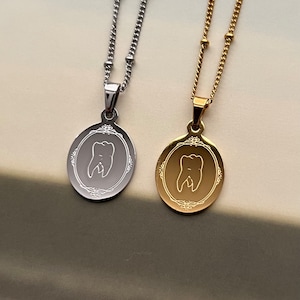May include: Two silver and gold necklaces with oval pendants featuring a tooth design. The pendants have a decorative border.