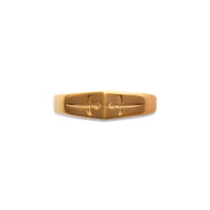 May include: A gold-toned ring featuring a central pointed design with two engraved sword motifs facing opposite directions. The band has a smooth, polished finish and a symmetrical shape that tapers towards the centre point on the front surface.