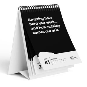 Könnte beinhalten: Ein weißer Schreibtischkalender mit schwarzer Spiralbindung. Die Kalenderseiten sind schwarz mit weißem Text, der lautet: „Amazing how hard you work... and how nothing comes out of it.“ Der Kalender zeigt Woche 41 im Oktober.