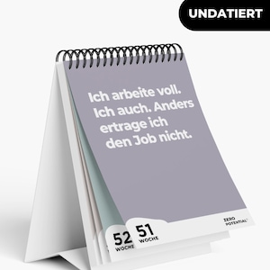 Pode incluir: Um calendário de mesa cinza com uma base branca e uma encadernação em espiral preta. O calendário apresenta o texto "Ich arbeite voll. Ich auch. Anders ertrage ich den Job nicht." e o texto "UNDATIERT" no topo. O calendário também tem os números "52" e "51" com a palavra "WOCHE" abaixo de cada número. O texto "ZERO POTENTIAL" é impresso na parte inferior do calendário.