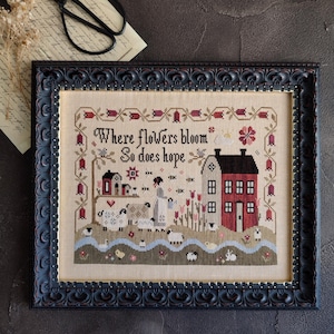 May include: Cross-stitch picture in a black frame, depicting a rural scene with a red and white house, sheep, and the text "Where flowers bloom, So does hope." The frame has an ornate design.