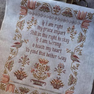 May include: A cross-stitch sampler on light fabric, featuring a poem with floral and bird motifs in muted tones of brown, peach, and green. The text reads, "If I am right thy grace impart..." The design includes flower baskets and decorative borders.