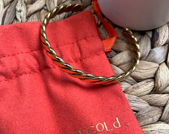 May include: A gold-colored twisted bangle bracelet in a red velvet pouch with the text "MARA THE GOLD" printed on the pouch.