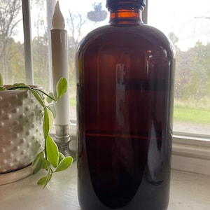 May include: A dark brown glass bottle with a dark brown cap. The bottle is filled with a dark liquid. The bottle is sitting on a white surface.