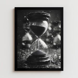 May include: Black and white framed print of an hourglass. The hourglass is made of clear glass with dark sand flowing from the top bulb to the bottom. The frame is black, and the background is blurred with water droplets.