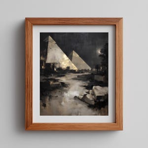 May include: Framed art print depicting two pyramids illuminated by a golden light, set against a dark night sky. The artwork features a river and landscape in shades of gray, brown, and gold. The print is encased in a natural wood frame.