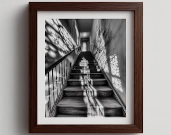 May include: Black and white framed photograph of a staircase. The image captures a long, ascending staircase with wooden steps and a metal railing. Shadows from a window create a pattern on the wall and steps.
