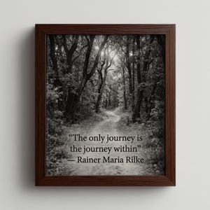 Può includere: Stampa in bianco e nero incorniciata con un sentiero nella foresta. La stampa include la citazione "L'unico viaggio è il viaggio interiore" di Rainer Maria Rilke. La cornice è marrone scuro.