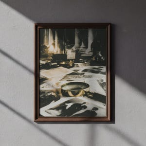 May include: A framed sepia-toned print featuring a desk scene with scattered papers, a magnifying glass, and other objects. The print has a dark brown frame and is set against a gray wall. The scene evokes a vintage, detective-like atmosphere.