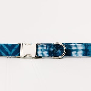 May include: A blue and white tie-dye dog collar with a silver buckle and a silver D-ring.
