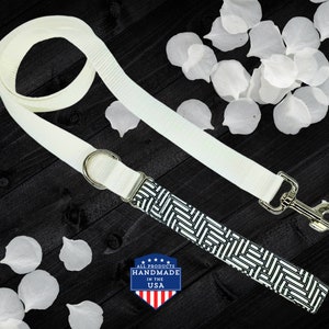 May include: White dog leash with a black and white geometric pattern. The leash has a silver clip and a silver D-ring. The leash is handmade in the USA.