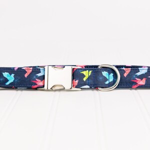 May include: A navy blue dog collar with a colorful origami bird pattern. The collar has a silver buckle and a silver D-ring.