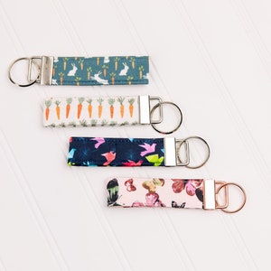 May include: Four keychains with different fabric patterns. The keychains are made of fabric with a variety of designs, including carrots, birds, butterflies, and bunnies. The keychains are attached to silver key rings.