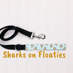 Requins en laisse pour chien flotteurs. Adorables requins portant un chapeau et tenant un verre sous un parapluie dans des flotteurs de piscine - Bleu pastel.