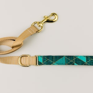 May include: A tan dog leash with a gold metal clip and a teal and gold geometric patterned fabric handle.