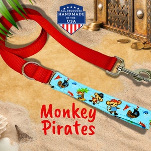 May include: Red dog lead with a blue and white fabric strap featuring a monkey pirate design. The strap has the text "Monkey Pirates" printed on it.