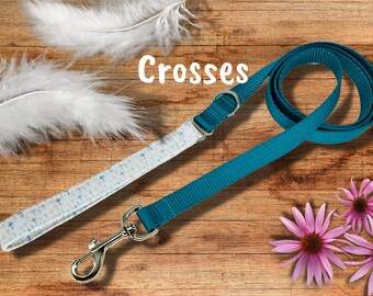 May include: A teal blue dog lead with a white lead featuring a pattern of small crosses. The leads are on a wooden surface with white feathers and pink flowers.