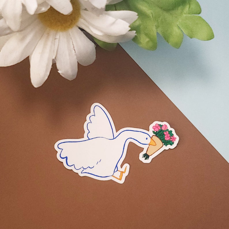 Pode incluir: Um adesivo de desenho animado de ganso branco com contornos azuis segurando um buqu&ecirc; de flores rosa em um cone de papel marrom.