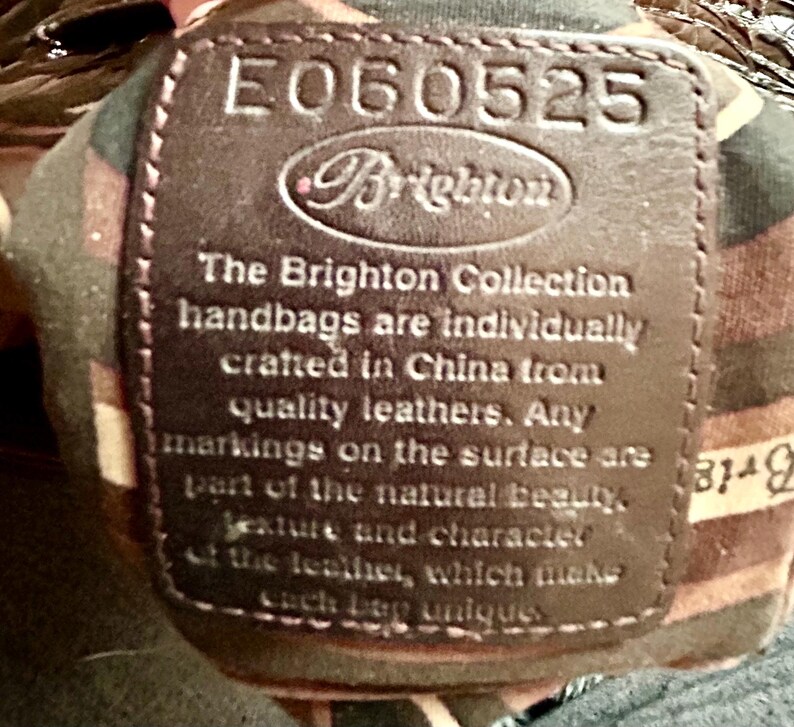 May include: A brown leather tag with the text "E060525 Brighton" and the text "The Brighton Collection handbags are individually crafted in China from quality leathers. Any markings on the surface are part of the natural beauty, texture and character of the leather, which makes each bag unique."