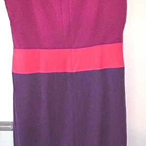 May include: Sleeveless dress in a color block design. The top section is a bright coral color, followed by a deep magenta band, then another coral band, and finally a deep purple skirt. The dress is hanging on a wooden hanger.