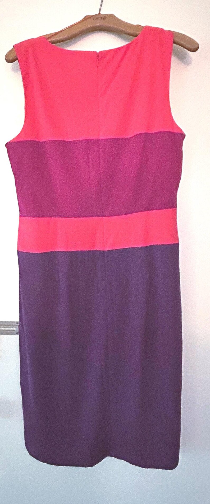 May include: Sleeveless dress in a color block design. The top section is a bright coral color, followed by a deep magenta band, then another coral band, and finally a deep purple skirt. The dress is hanging on a wooden hanger.