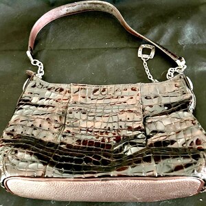 May include: A brown crocodile embossed leather handbag with a silver chain strap and a silver charm.