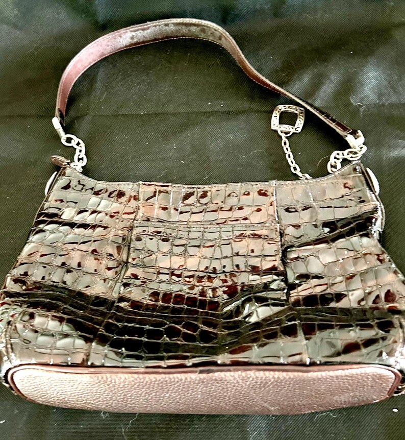 May include: A brown crocodile embossed leather handbag with a silver chain strap and a silver charm.