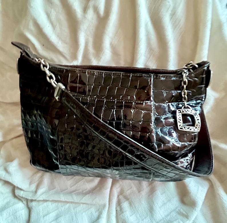 May include: A brown crocodile embossed leather handbag with a silver chain strap and a silver charm. The bag has a flap closure and a top handle.