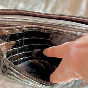 May include: The inside of a black crocodile-embossed purse with a zipper closure. The purse has a smooth, shiny finish.
