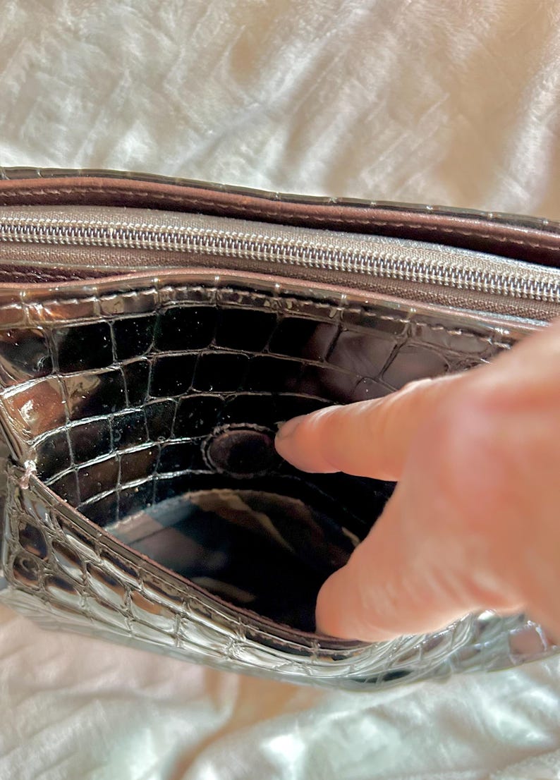 May include: The inside of a black crocodile-embossed purse with a zipper closure. The purse has a smooth, shiny finish.