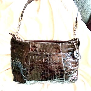 May include: A brown crocodile embossed leather handbag with a silver chain strap and a silver charm.