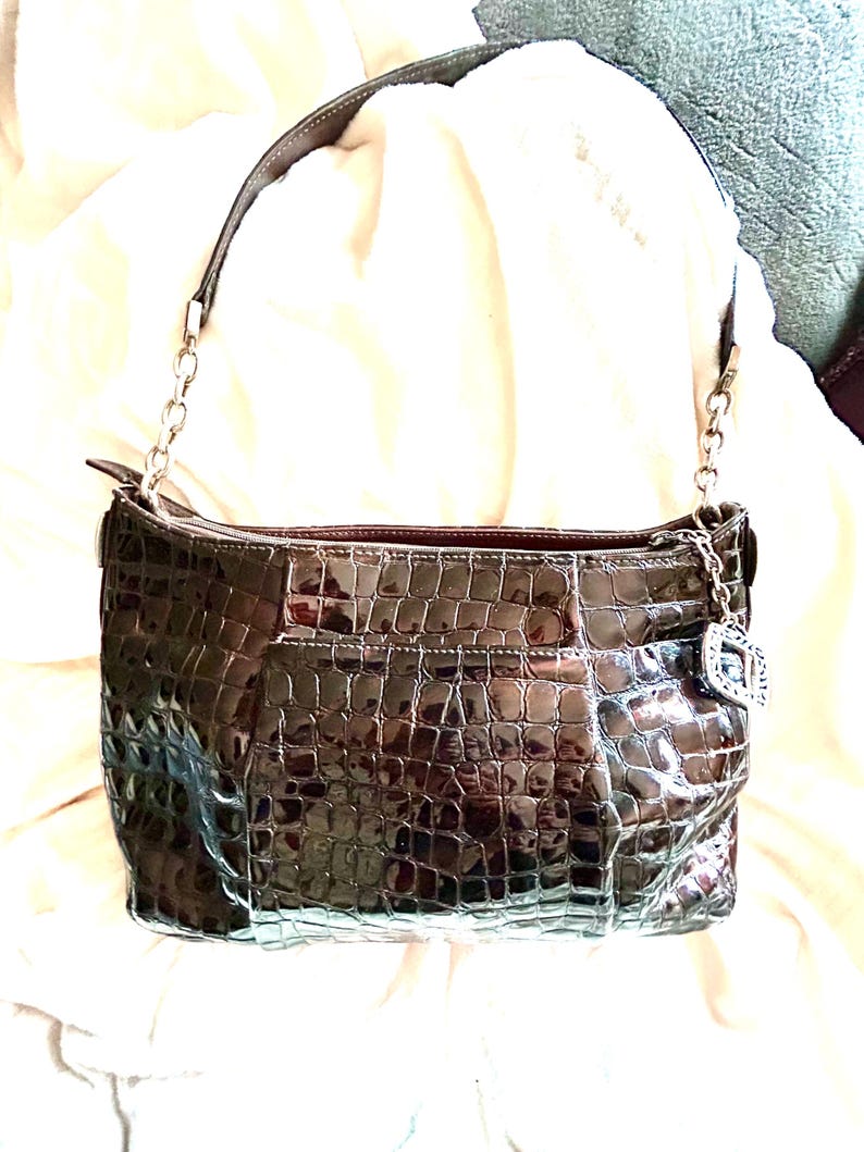 May include: A brown crocodile embossed leather handbag with a silver chain strap and a silver charm.