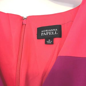 May include: A close-up of a color-blocked dress with a zipper. The dress features shades of pink and purple. The label reads "ADRIANNA PAPELL" and indicates a size 14, made in China.