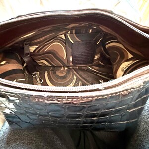 May include: A black crocodile embossed leather handbag with a brown and cream patterned lining. The lining has a zippered pocket and a small leather tag that reads "Brighton".