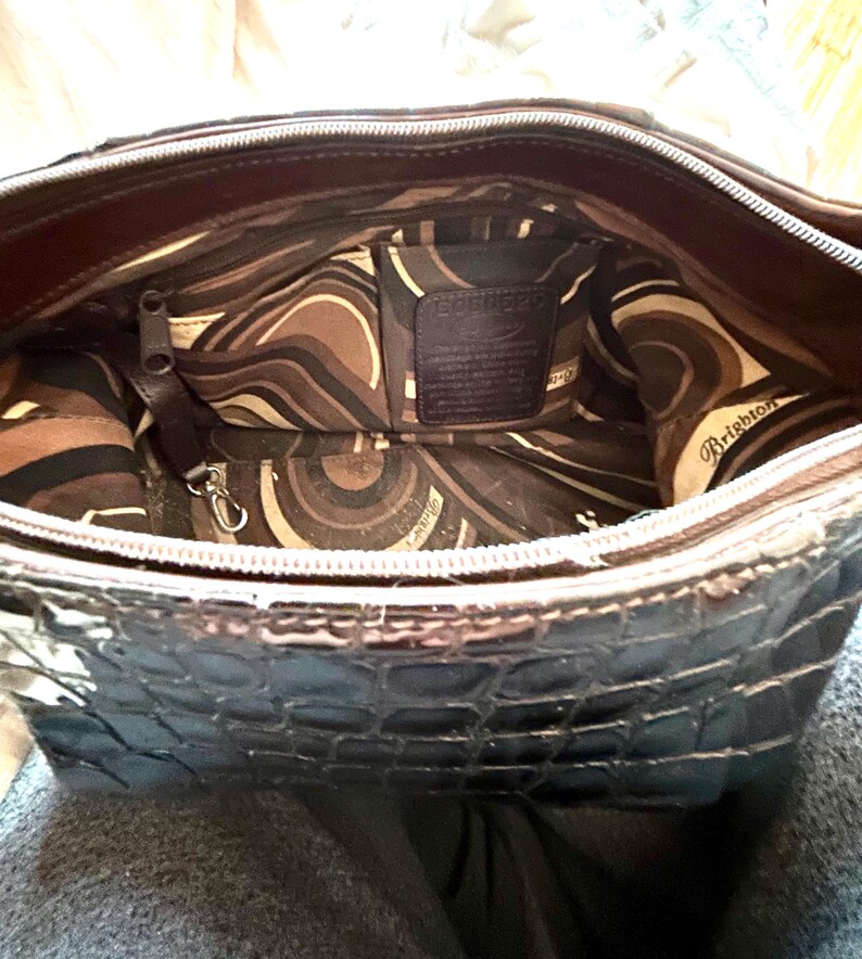 May include: A black crocodile embossed leather handbag with a brown and cream patterned lining. The lining has a zippered pocket and a small leather tag that reads "Brighton".
