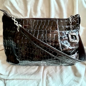 May include: A brown crocodile embossed leather handbag with a silver chain strap and a silver clasp.