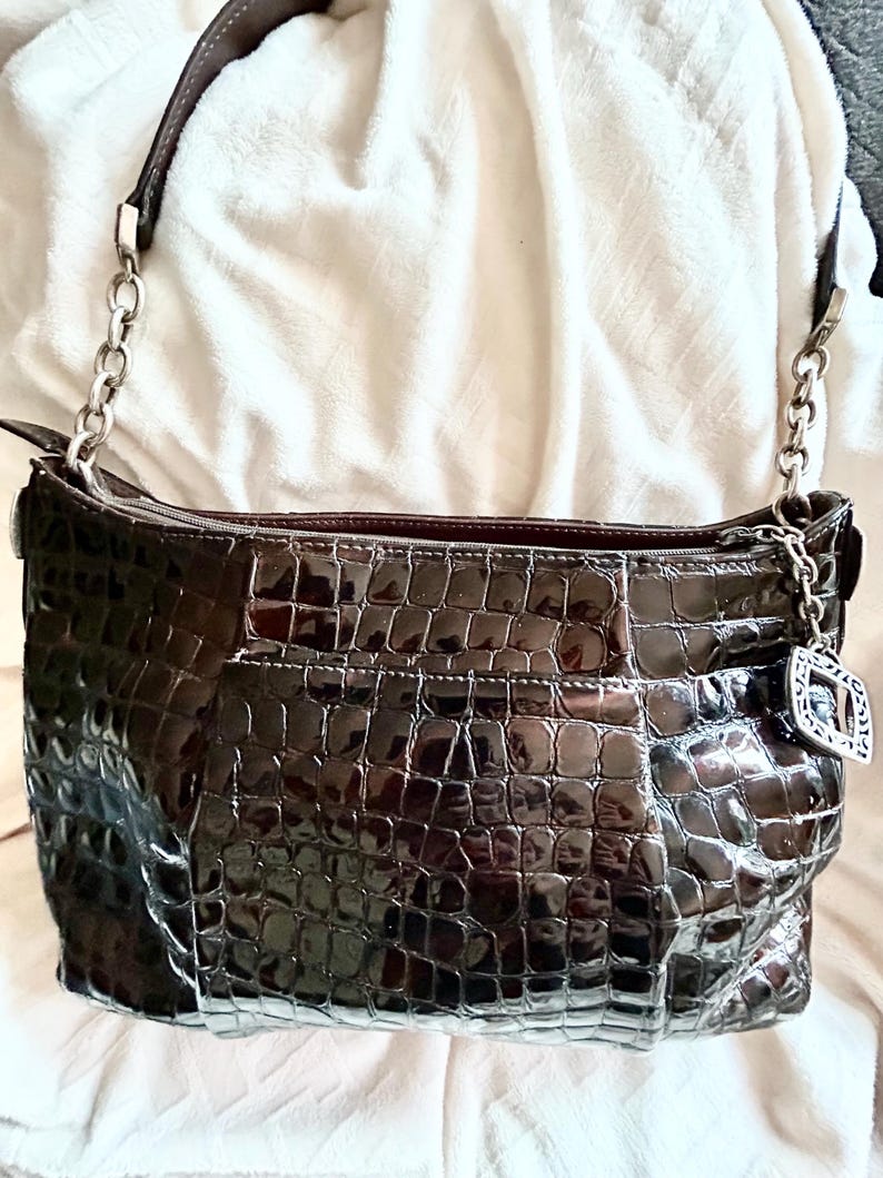 May include: A brown crocodile embossed leather handbag with a silver chain strap and a silver charm.