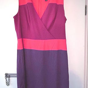 May include: Sleeveless color block dress in shades of red, fuchsia, and purple. The dress features a V-neckline and a knee-length hem. The brand name "Adrianna Papell" is visible on a tag near the neckline. The dress is hanging on a wooden hanger.