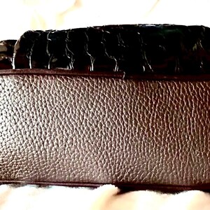May include: A brown leather handbag with a crocodile-embossed design. The bag has a smooth, textured bottom.